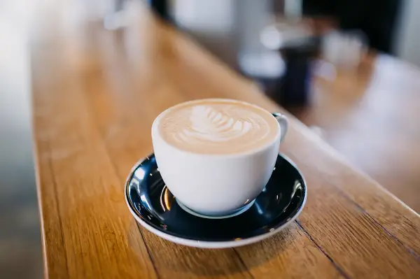 A cup of coffee with latte art served on a wooden table in a black saucer
