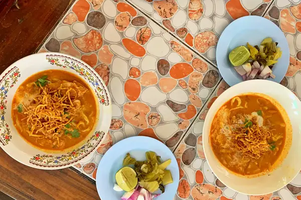 Three servings of noodles in broth with toppings on ornate plates accompanied by small dishes of garnishes and spices