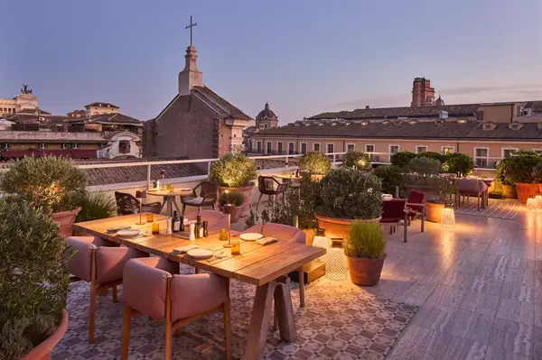 Rooftop bar and dining setting with urban and church views in a cityscape backdrop, evening lighting enhances the atmosphere