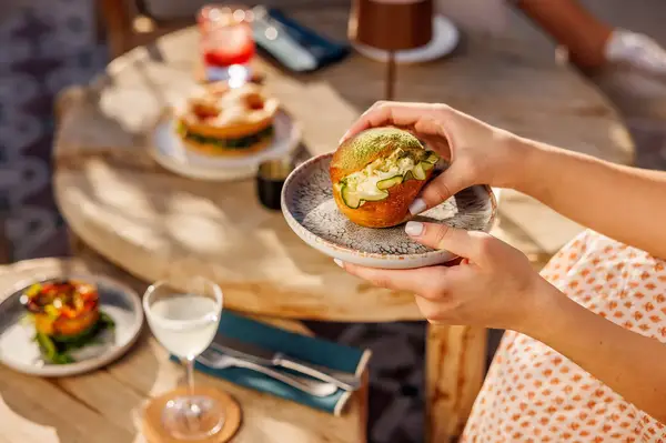 A person holding a plate with a dish, a table set with food and drinks in the background