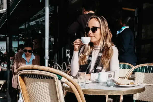 A person sitting at an outdoor caf table sipping from a cup