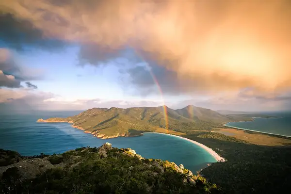 An aerial view of a coastal landscape with a rainbow over hills and beaches