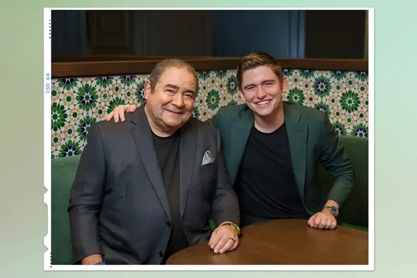 Emeril Lagasse seated next to a smiling young man at a table.