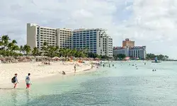 Resort buildings along a beach with people swimming and walking by the water