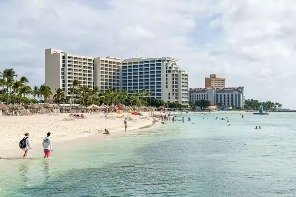 Resort buildings along a beach with people swimming and walking by the water