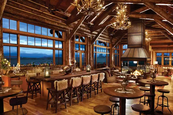 Interior of a luxurious lodge with a bar counter and seating area featuring large windows and a rustic ambiance