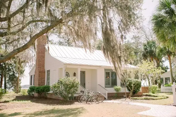 A white house with a porch surrounded by trees and landscaping, two bicycles parked in front