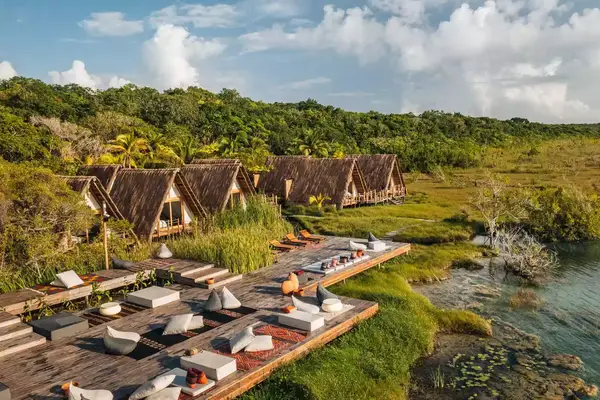 Exterior view of Habitas Bacalar in Mexico with lounge chairs on a wood deck along the water