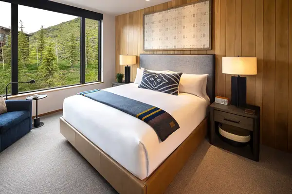 A cozy bedroom with a modern design featuring a bed nightstands and a large window overlooking green foliage