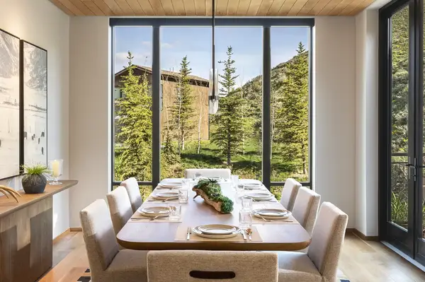Dining table arranged in a modern penthouse surrounded by windows overlooking a green landscape