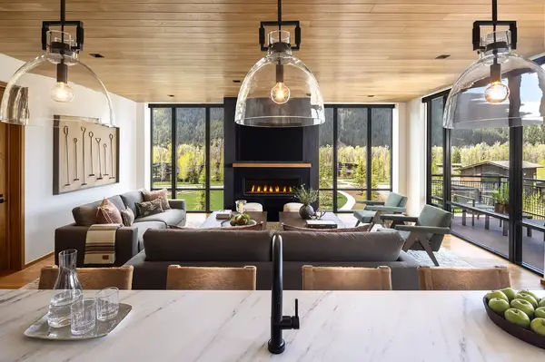 Interior of living and dining area with large windows overlooking a natural setting a fireplace and modern decor