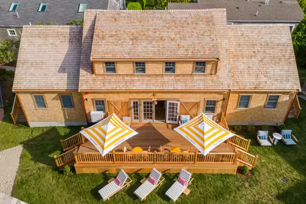 aerial view of a wood house with yellow stripped umbrellas on the patio and white lawn chairs on the grass below