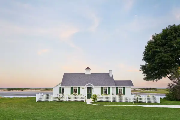 shot of a small white house with green door and window shutters at sunset