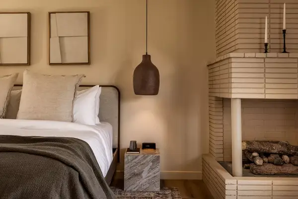 interior of a guest room with white sheets and a small fireplace to the right and warm beige walls