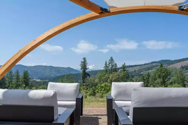 Outdoor lounge seating under a wooden archway, overlooking a scenic landscape with mountains and trees