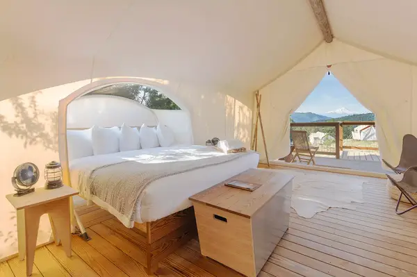 Interior view of a tent featuring a bed, wooden furniture, and an outdoor deck overlooking nature