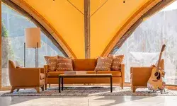 A cozy living area with an arrangement of chairs, a sofa, and a coffee table, set under a canvas structure with a scenic backdrop