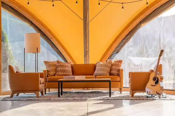 A cozy living area with an arrangement of chairs, a sofa, and a coffee table, set under a canvas structure with a scenic backdrop