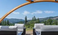Outdoor lounge seating under a wooden archway, overlooking a scenic landscape with mountains and trees