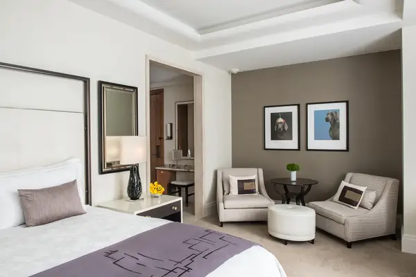 A luxurious hotel room with a bed two armchairs and a lamp on a side table