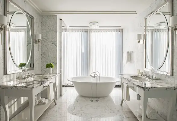 Luxurious bathroom with a central freestanding bathtub dual vanities large mirrors and sheer curtains over tall windows