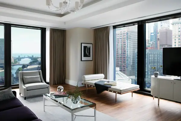 A modern living room with large windows overlooking a cityscape featuring a sofa armchair glass coffee table and a chaise lounge