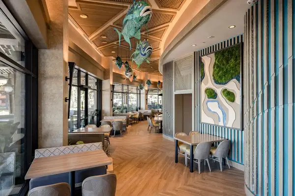 An interior view of a restaurant featuring wooden floors tables and unique Polynesianthemed decorations hanging from the ceiling