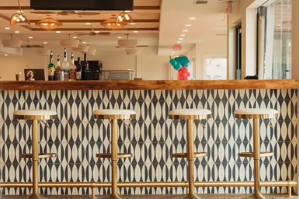 A bar counter with four stools in an empty space, geometric tile design on the bar front