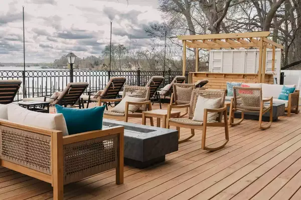 Outdoor seating area with chairs, tables, and a bar on a wooden deck overlooking a body of water