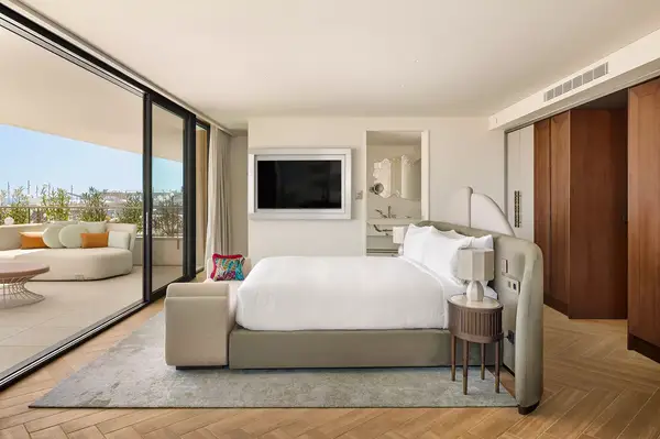 A hotel guestroom with a bed, built-in TV, and access to a balcony with outdoor seating