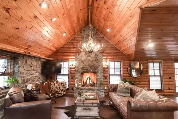 A cozy rustic room with a central stone fireplace, wooden ceiling, and leather furniture