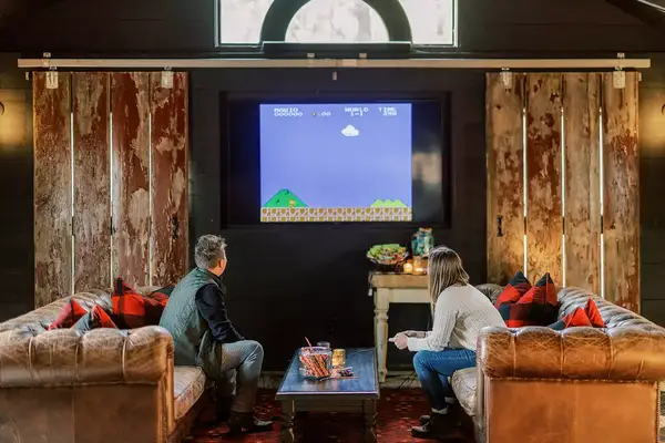 Two people sitting in a cozy room playing a video game on a large screen