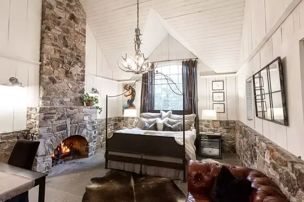 A cozy bedroom with a stone fireplace, rustic decor, and a chandelier