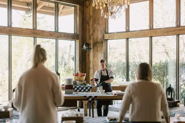 A cooking class led by an instructor wearing an apron, seen working at a table in a well-lit rustic space with large windows