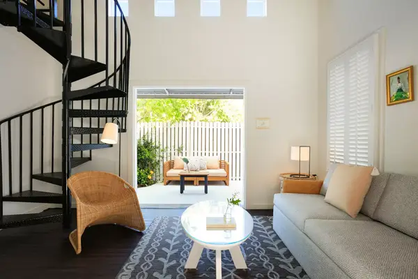 Spiral staircase, modern living room with sofa and table, door leading to outdoor patio with seating area.