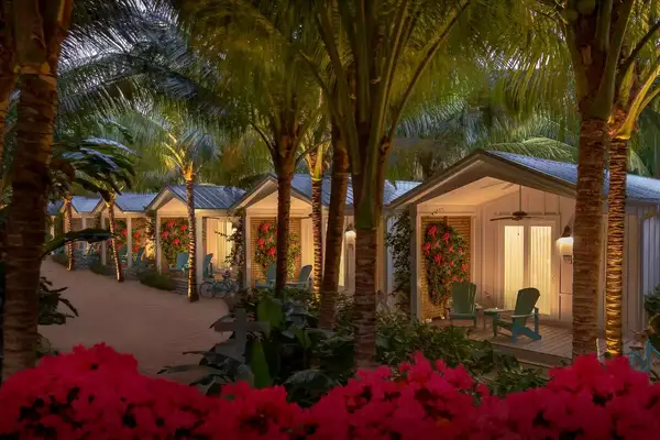 Bungalows surrounded by palm trees, tropical plants, and flowers, with patios and seating areas visible at night.