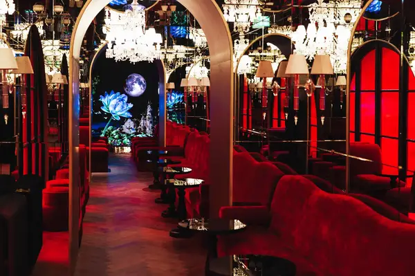 Elegant interior of a venue with red seating and chandeliers, arches lead to an illuminated art backdrop featuring a moon and flowers