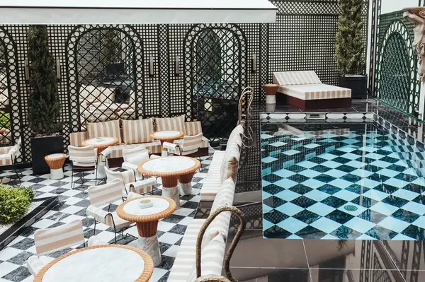 An elegant poolside area with checkerboard flooring, striped furniture, and a lush garden setting, with a contemporary design and seating