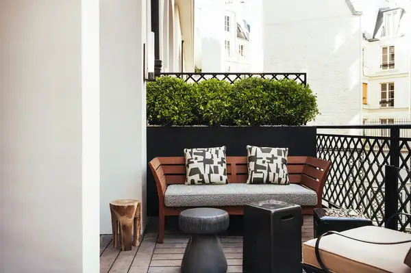 Outdoor terrace seating with a wooden bench and decorative pillows, surrounded by city buildings