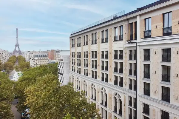 An exterior view of a building in Paris with the Eiffel Tower in the distance, surrounded by a tree-lined street