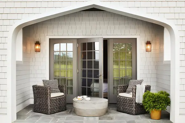 A cottage outdoor seating area with a round table and two chairs arranged on a patio