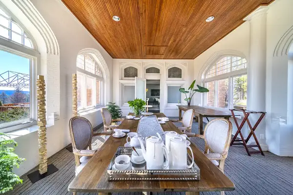 A serene tea room with a wooden ceiling, large windows, a set table with a tea set, and chairs arranged around the table