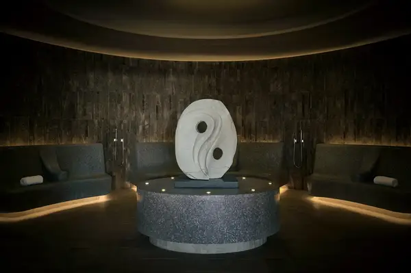 A spa room with a sculpted centerpiece under dim lighting, featuring curved seating areas