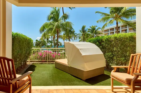 Outdoor seating area with a canopy sunbed, surrounded by greenery and palm trees