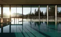 Indoor pool with large glass windows overlooking a mountain forest landscape sunlight streaming through the windows