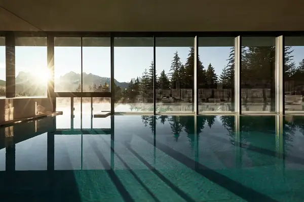 Indoor pool with large glass windows overlooking a mountain forest landscape sunlight streaming through the windows