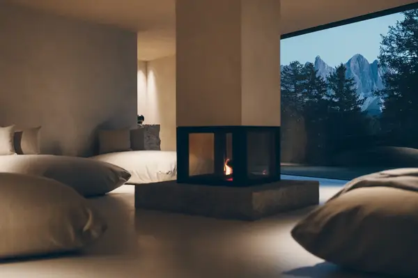 Modern lounge area with large cushions central fireplace and a window overlooking mountain scenery