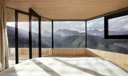 Panoramic mountain view from a minimalist room with large windows and wooden interior