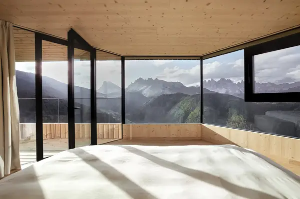 Panoramic mountain view from a minimalist room with large windows and wooden interior