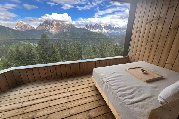 Wooden balcony with a bed overlooking a mountainous forest landscape